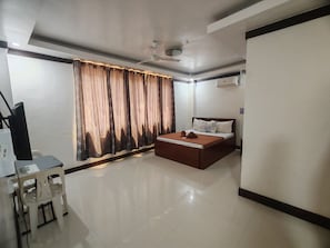 Una habitación de hotel con una cama, un escritorio con silla, un ventilador de techo y cortinas.