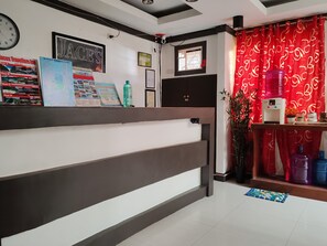A reception desk with a clock, framed posters, a water dispenser, and a red curtain. - Jace's Travellers Inn By Zuzu (El Nido)