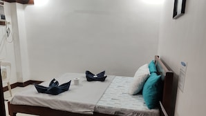 A single bed with a white bedspread, two pillows, a small bedside table with a remote control, and a wall-mounted air conditioning unit. - Jace's Travellers Inn By Zuzu (El Nido)