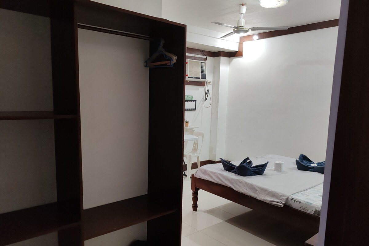 Un dormitorio con una cama, un armario, un ventilador de techo y una pequeña mesa con una silla.