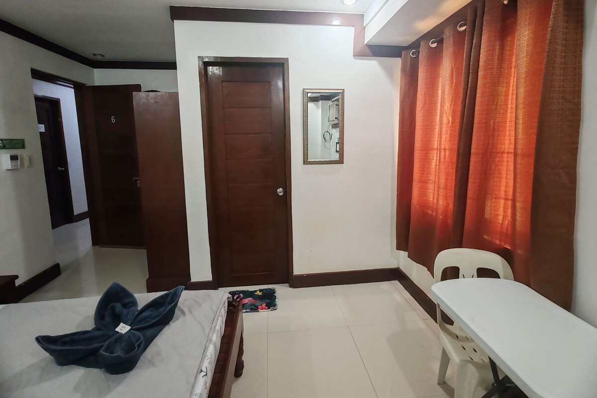 Habitación de hotel con cama, escritorio, silla, puerta y espejo.