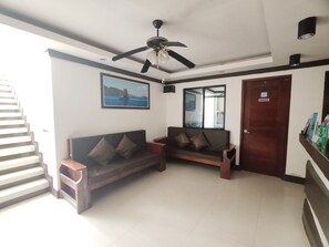 A spacious room with a ceiling fan, a sofa with cushions, a framed picture on the wall, a mirror, and a door with a sign. - Jace's Travellers Inn By Zuzu (El Nido)
