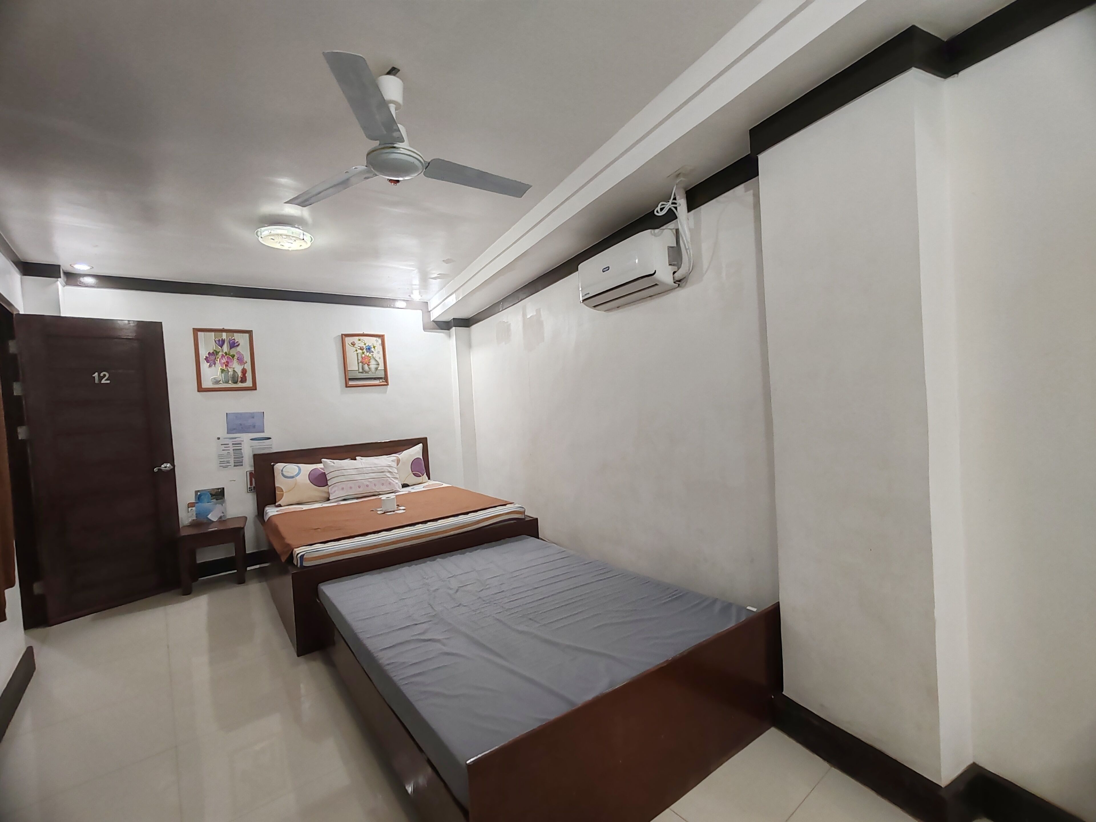Une chambre à coucher comprenant un lit, un ventilateur de plafond, un appareil de climatisation et une porte portant le numéro 12.