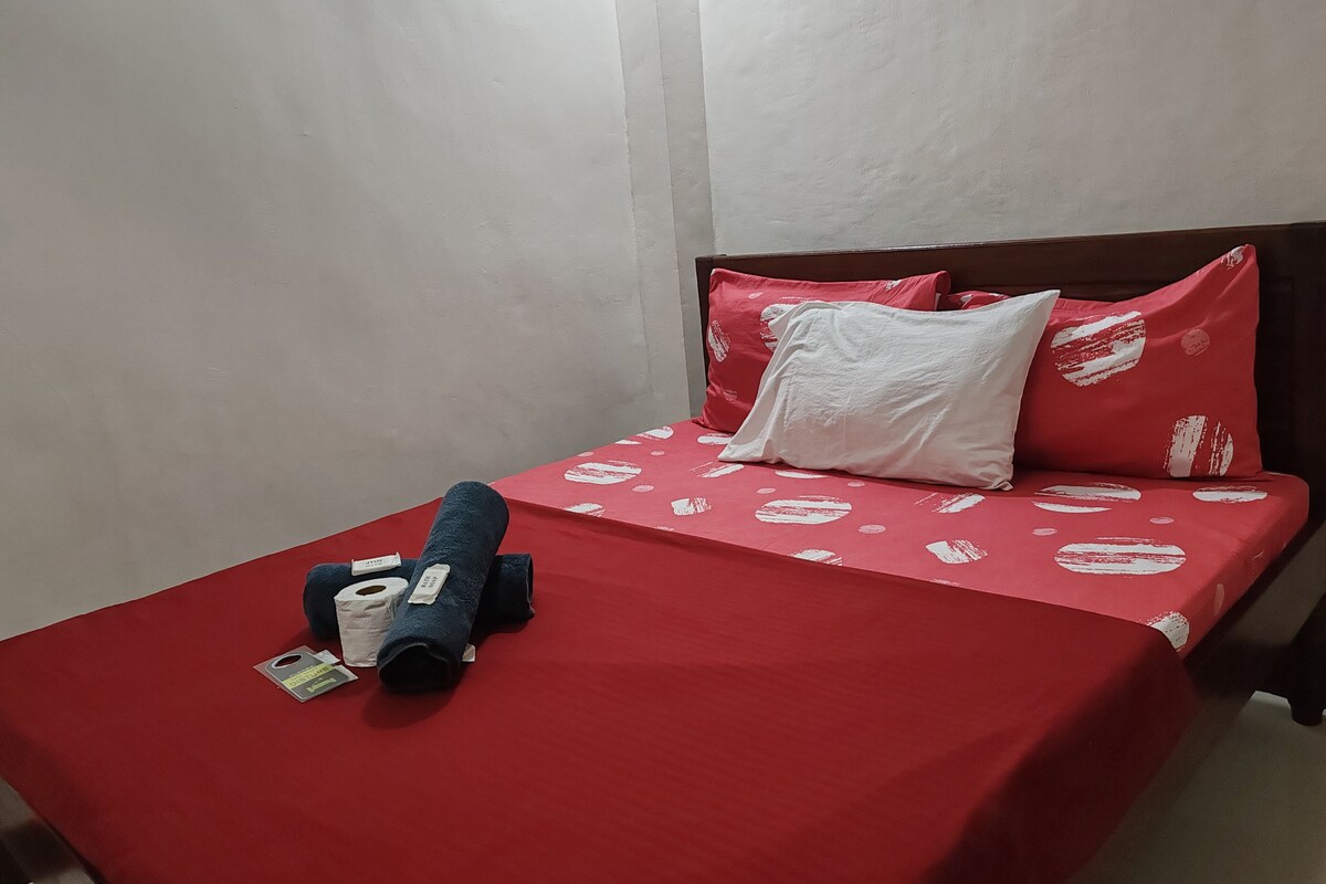 A bed with a red bedspread, a white pillow, and a rolled-up blanket.