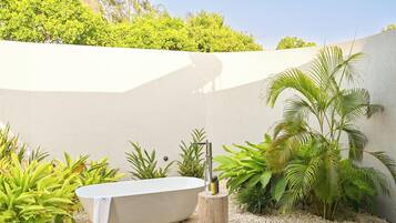 A spa area with a freestanding bathtub, surrounded by tropical plants and a white wall.