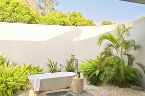 A spa area with a freestanding bathtub, surrounded by tropical plants and a white wall. - Bawe Island Resort (Bawe Island)