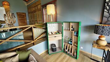 Una habitación con cama estilo altillo, un mueble de almacenamiento verde con botellas, una lámpara colgante y una escalera de madera.