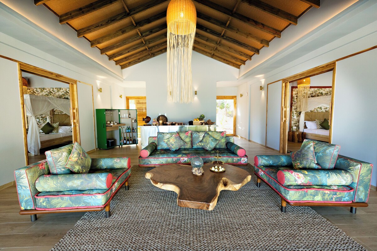 A spacious living area with a large sofa set, a coffee table, and a high ceiling with wooden beams.