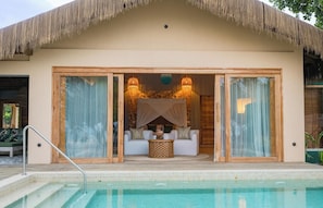 A poolside lounge with a thatched roof, a seating area with cushions, and a pool. - Bawe Island Resort (Bawe Island)