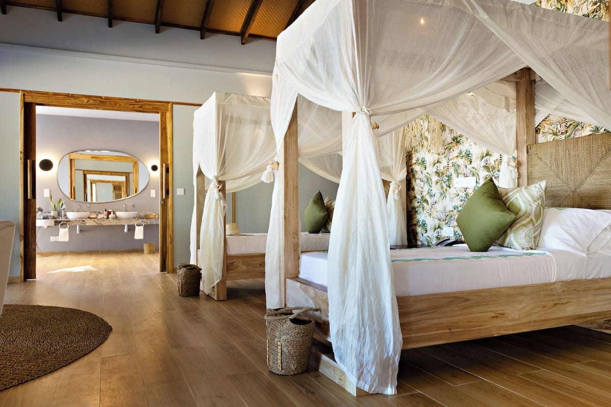 A bedroom with a canopy bed, a bathroom with a mirror and sink, and a wooden floor.