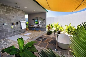 A modern outdoor bathroom with a stone floor, a large sink, a bathtub, and a mirror. - Bawe Island Resort (Bawe Island)