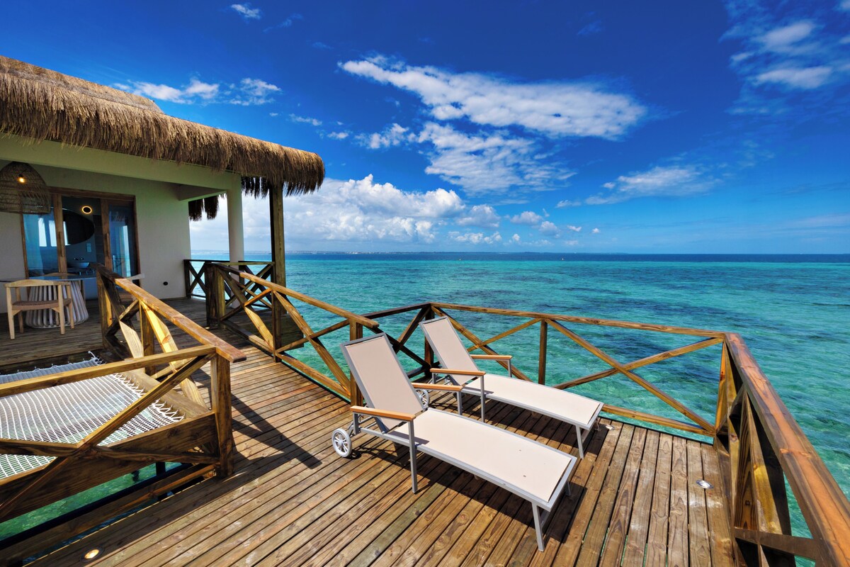 A wooden deck with lounge chairs and a thatched-roof structure.