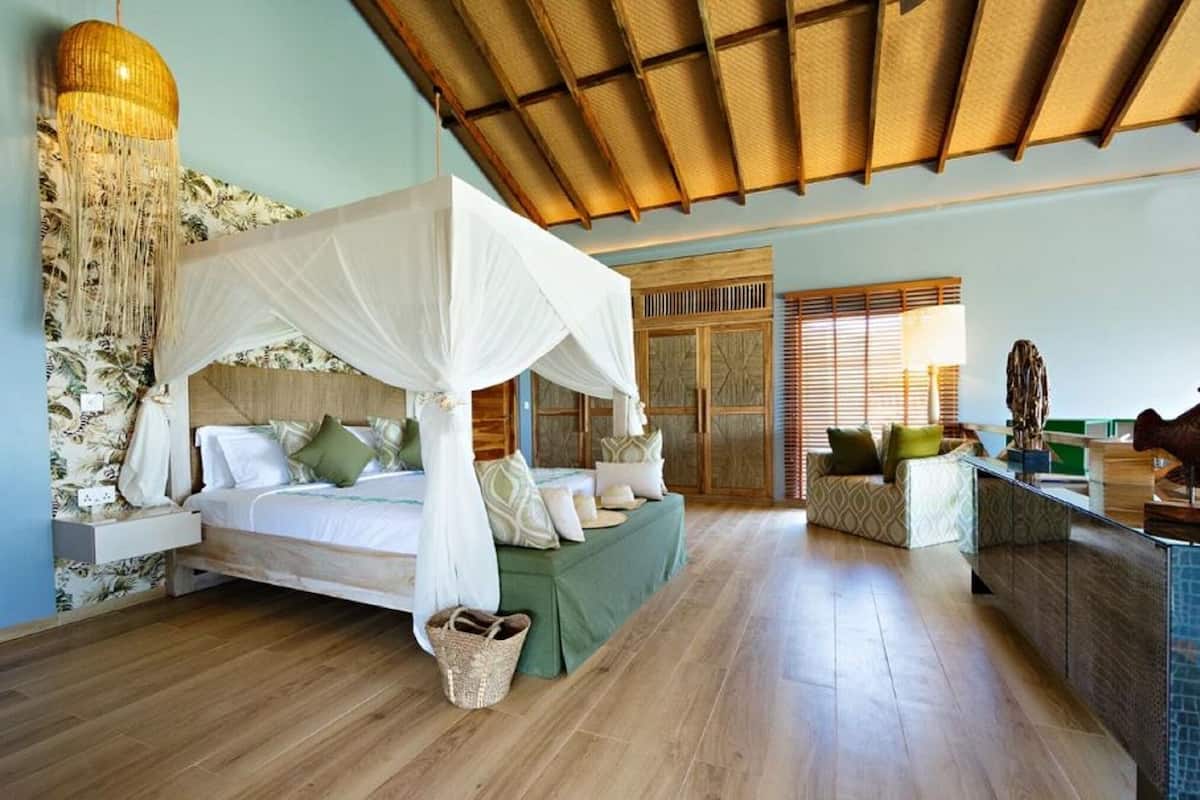 A bedroom with a canopy bed, a sitting area with a sofa, a wooden ceiling, and a large decorative hanging light.
