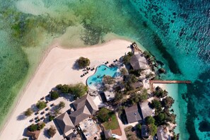 An aerial view of a resort with a swimming pool, beach, and clear turquoise waters. - Bawe Island Resort (Bawe Island)