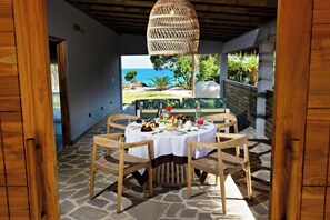A table set for breakfast with wicker chairs, a hanging light, and a view of the ocean. - Bawe Island Resort (Bawe Island)