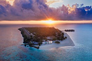An aerial view of a tropical island resort with a beach, clear waters, and a sunset. - Bawe Island Resort (Bawe Island)