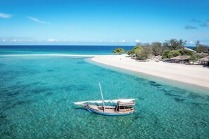A boat anchored near a beach with clear turquoise water, a sandy shore, and overwater bungalows. - Bawe Island Resort (Bawe Island)