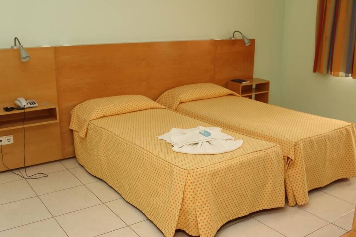 A room with two beds, a bedside table, a lamp, a phone, and a curtain.