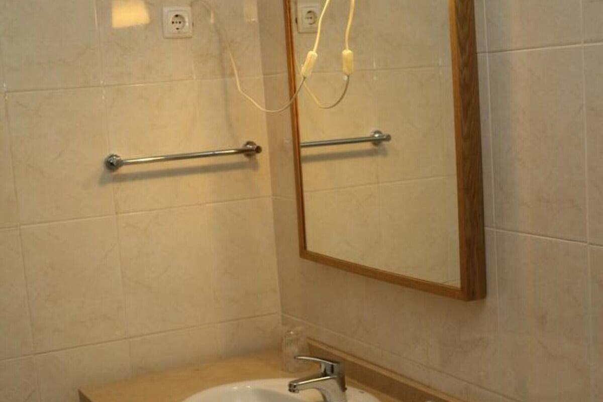 A bathroom with a sink, mirror, towel rack, and wall-mounted light fixture.