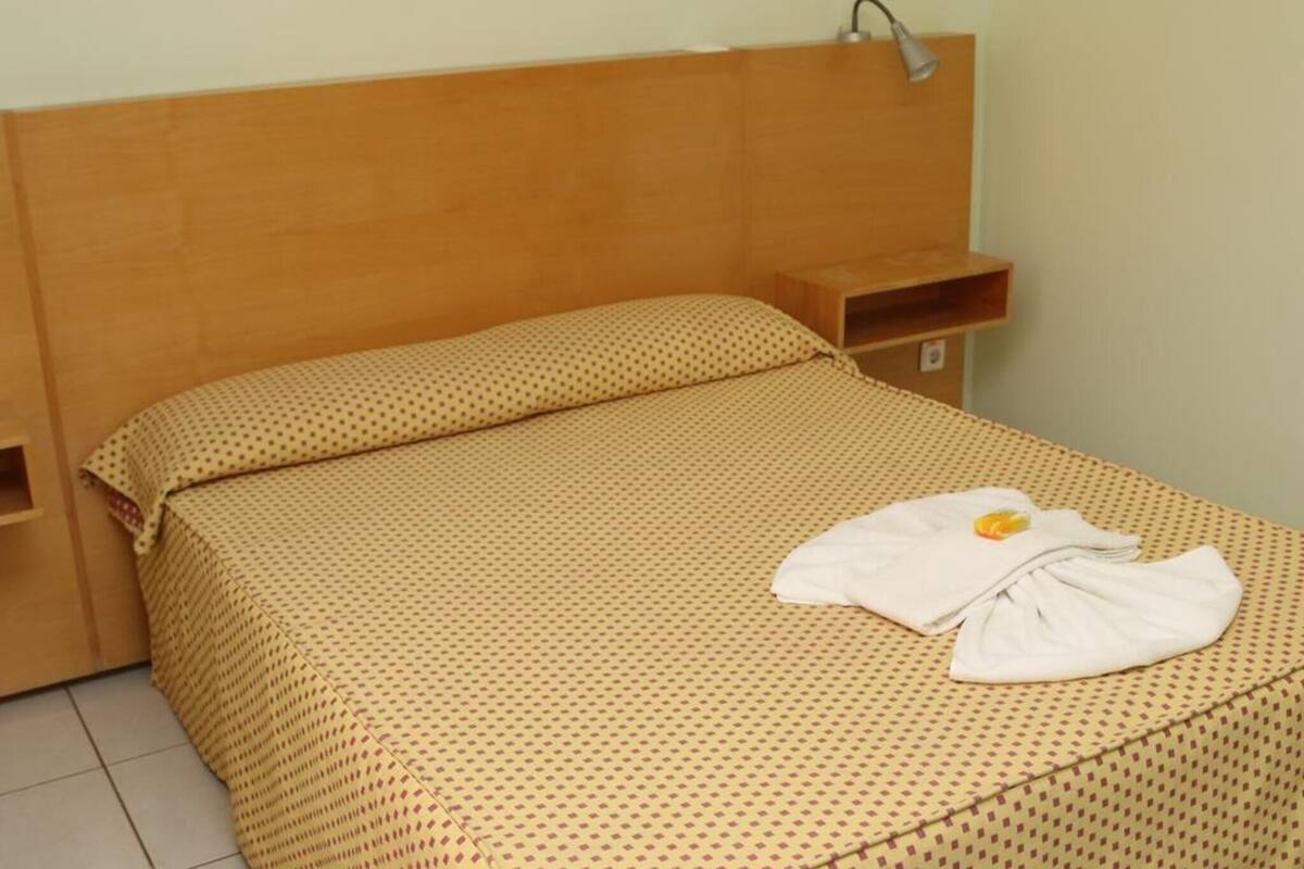 A single bed with a headboard, a bedside table, and a wall-mounted lamp.