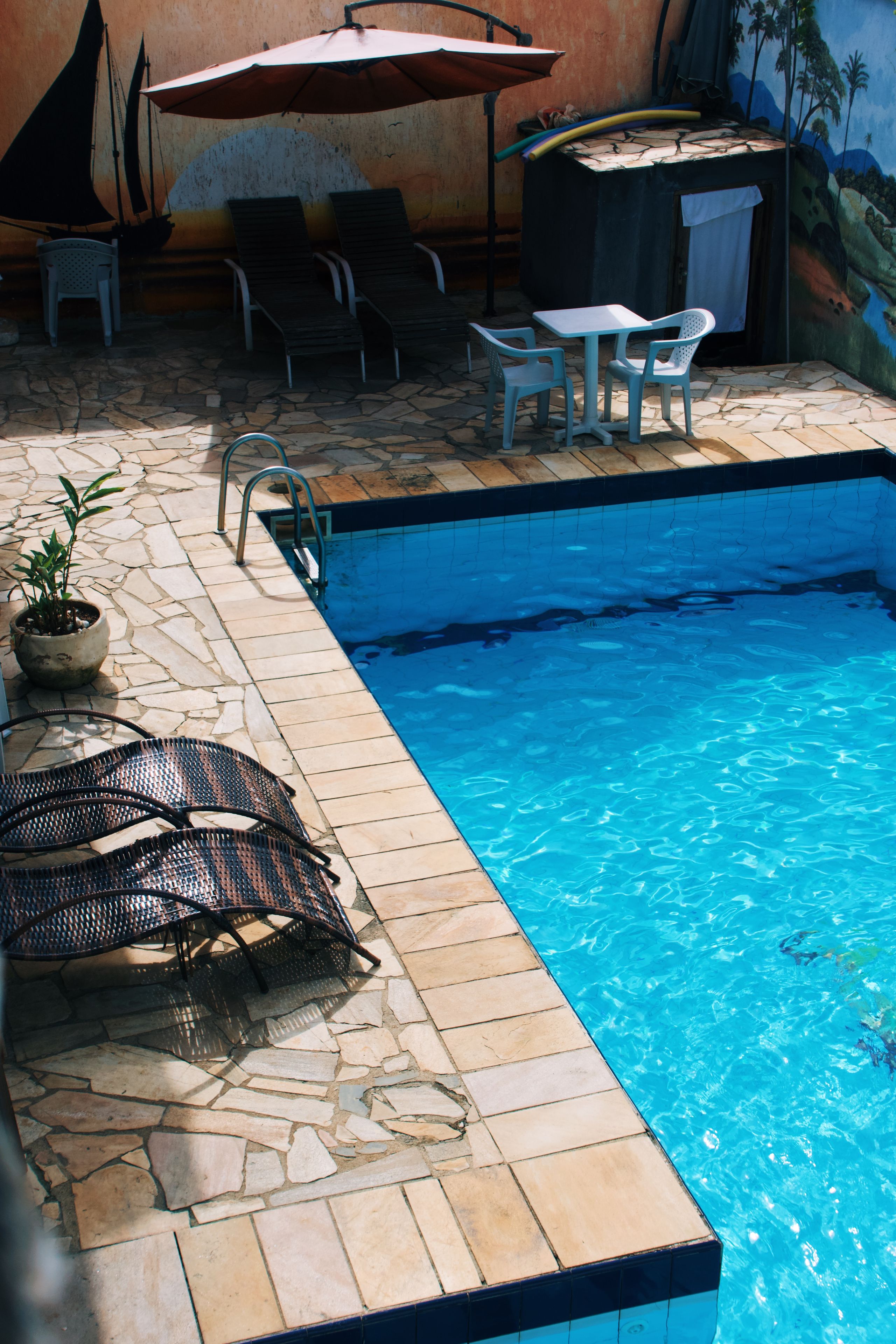 A swimming pool with lounge chairs and a table, surrounded by stone tiles and a mural.