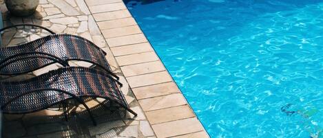A swimming pool with lounge chairs and a table, surrounded by stone tiles and a mural.