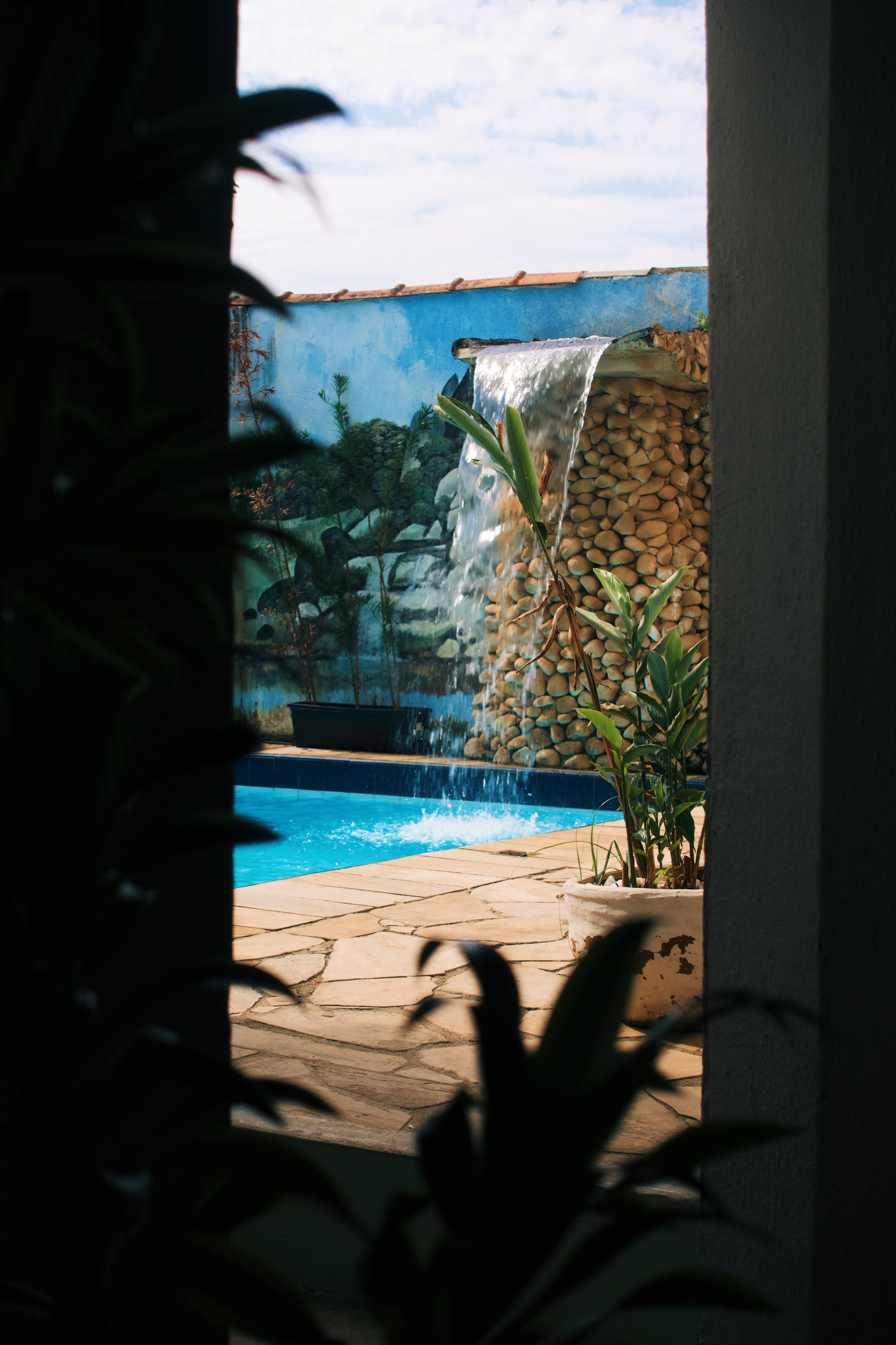 Ein Pool mit Wasserfall, umgeben von Pflanzen und einer Steinmauer.