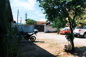 Zona residencial con una motocicleta estacionada sobre tierra, una camioneta pickup blanca y un árbol en primer plano.