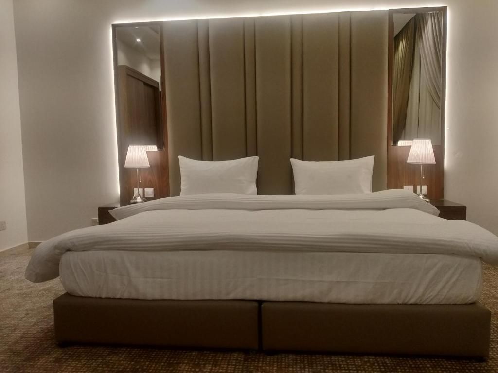 A hotel room with a large bed, two bedside lamps, and a mirror above the bed.