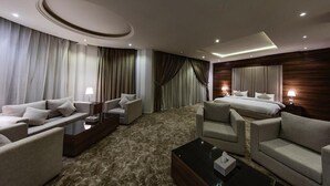 Quarto de hotel com uma cama grande, dois sofás, uma mesa de centro e uma televisão.