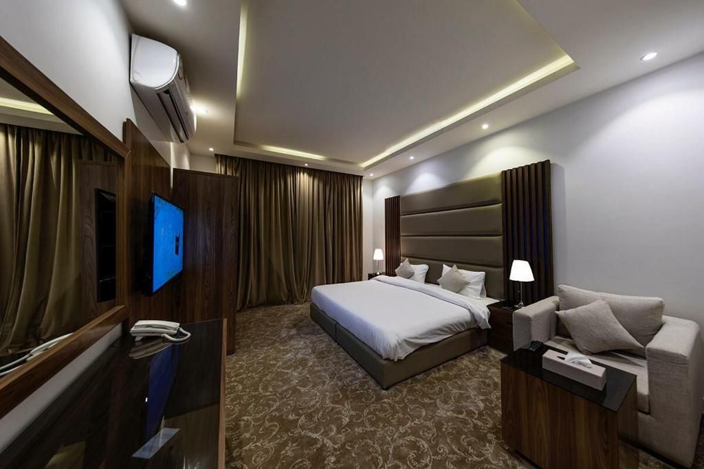 Ein Hotelzimmer mit einem großen Bett, einem Nachttisch mit Lampe, einem Fernseher und einem Spiegel.