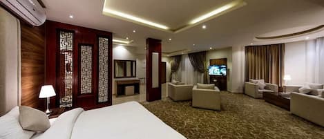 A hotel room with a large bed, two sofas, a TV, and a decorative wall panel.