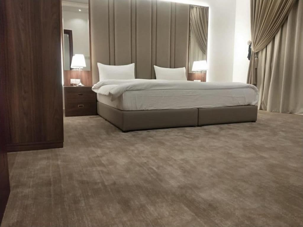 A hotel room with a large bed, a nightstand, a mirror, and a window with curtains.