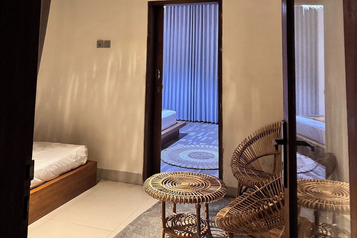 A room with a bed, a small round table, and two wicker chairs.