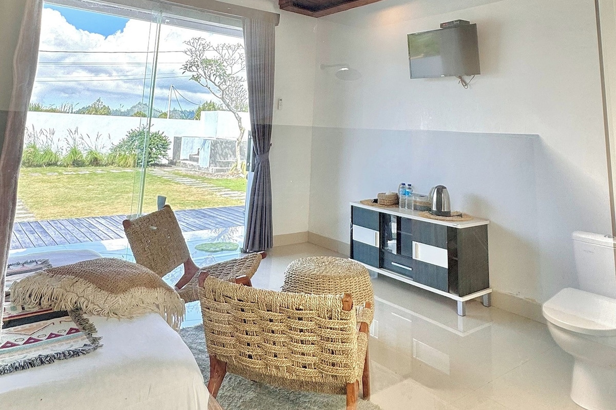 A bedroom with a bed, two wicker chairs, a small cabinet, and a toilet.