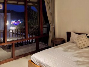 A bedroom with a large window, a bed with white bedding, a wooden headboard, and a small wicker stool. - Volcano Side Kintamani Bali By Zuzu (Kintamani)