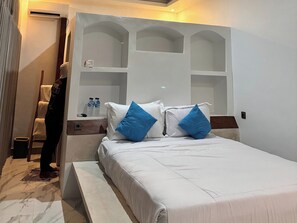 A hotel room with a bed, a nightstand, a shelf with bottles, and a towel rack. - Volcano Side Kintamani Bali By Zuzu (Kintamani)