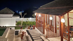 A modern outdoor area with a pool, wooden deck, and seating area with hanging lights. - Volcano Side Kintamani Bali By Zuzu (Kintamani)