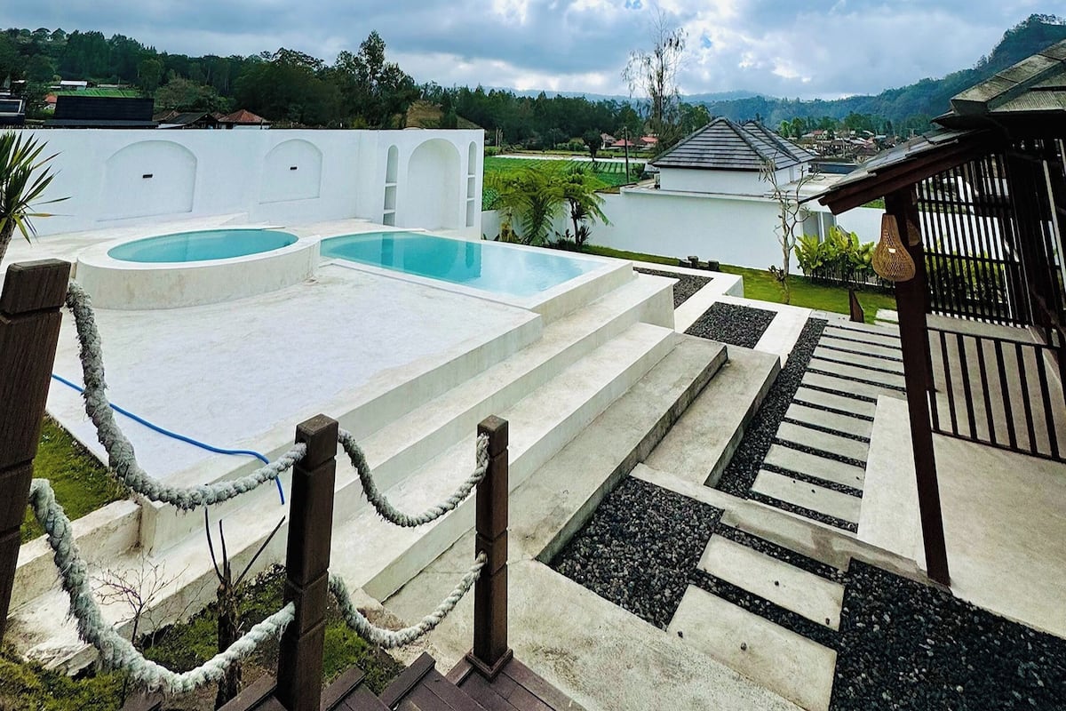 Piscina com degraus de acesso, cercada por um muro branco e uma cerca de madeira.
