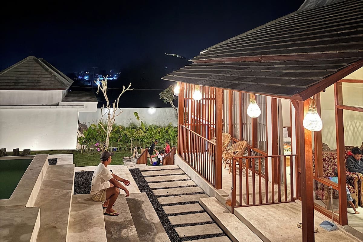 Uma área externa moderna com piscina, deck de madeira e espaço de estar com luzes pendentes.