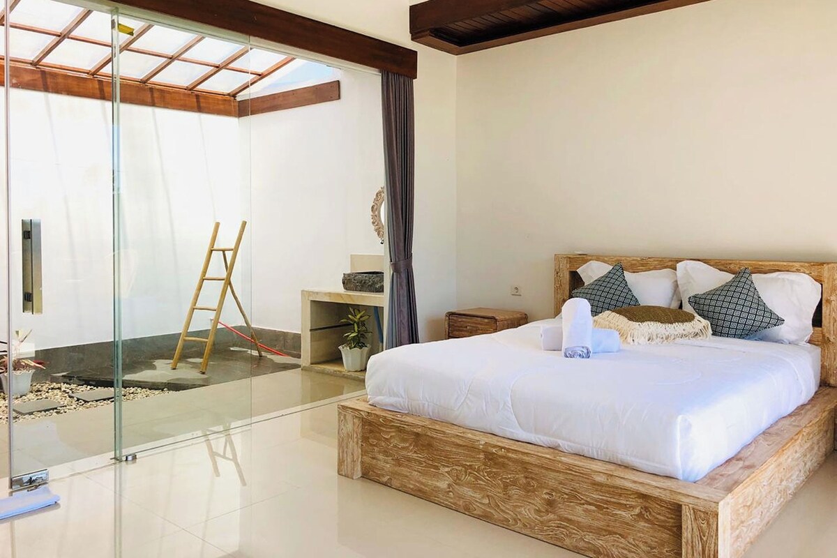 A modern bedroom with a glass door leading to a balcony, a wooden bed frame, and a small bedside table.