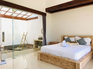A modern bedroom with a glass door leading to a balcony, a wooden bed frame, and a small bedside table. - Volcano Side Kintamani Bali By Zuzu (Kintamani)