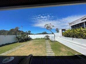 A covered outdoor area with a grassy lawn, a stone pathway, and a white wall. - Volcano Side Kintamani Bali By Zuzu (Kintamani)