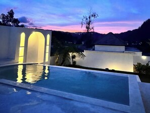 A swimming pool with a view of a sunset and a building with illuminated arches. - Volcano Side Kintamani Bali By Zuzu (Kintamani)