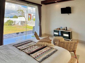 A bedroom with a large bed, a television on the wall, a small cabinet, and a view of the outdoors. - Volcano Side Kintamani Bali By Zuzu (Kintamani)