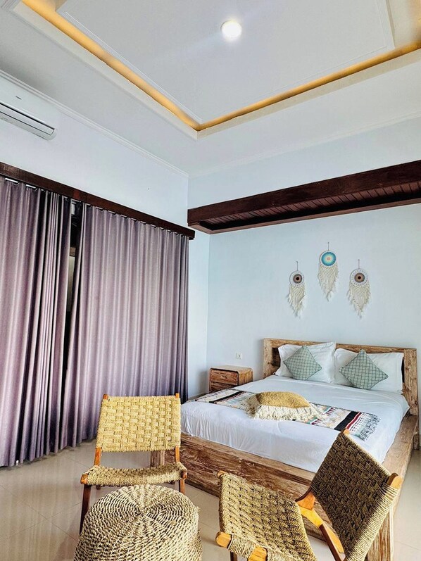 A bedroom with a bed, two woven chairs, a nightstand, and a wall with decorative elements. - Volcano Side Kintamani Bali By Zuzu (Kintamani)