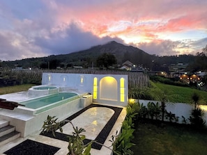 A spa area with a pool, a hot tub, and a sauna, surrounded by a white wall with arched windows and a view of a mountain. - Volcano Side Kintamani Bali By Zuzu (Kintamani)