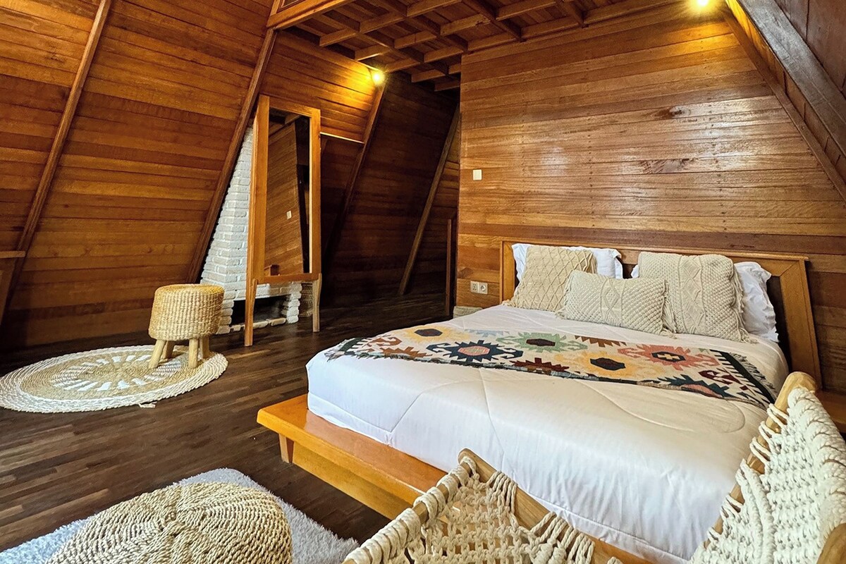 A wooden interior with a bed, a small seating area, and a staircase.