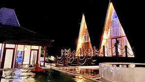 A pool area with a water slide, a building with large windows, and a structure with a pointed roof. - Volcano Side Kintamani Bali By Zuzu (Kintamani)