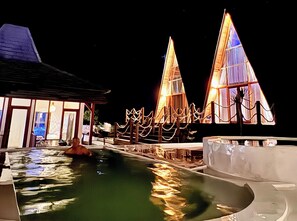 A pool area with a water slide, a building with large windows, and a structure with a pointed roof. - Volcano Side Kintamani Bali By Zuzu (Kintamani)